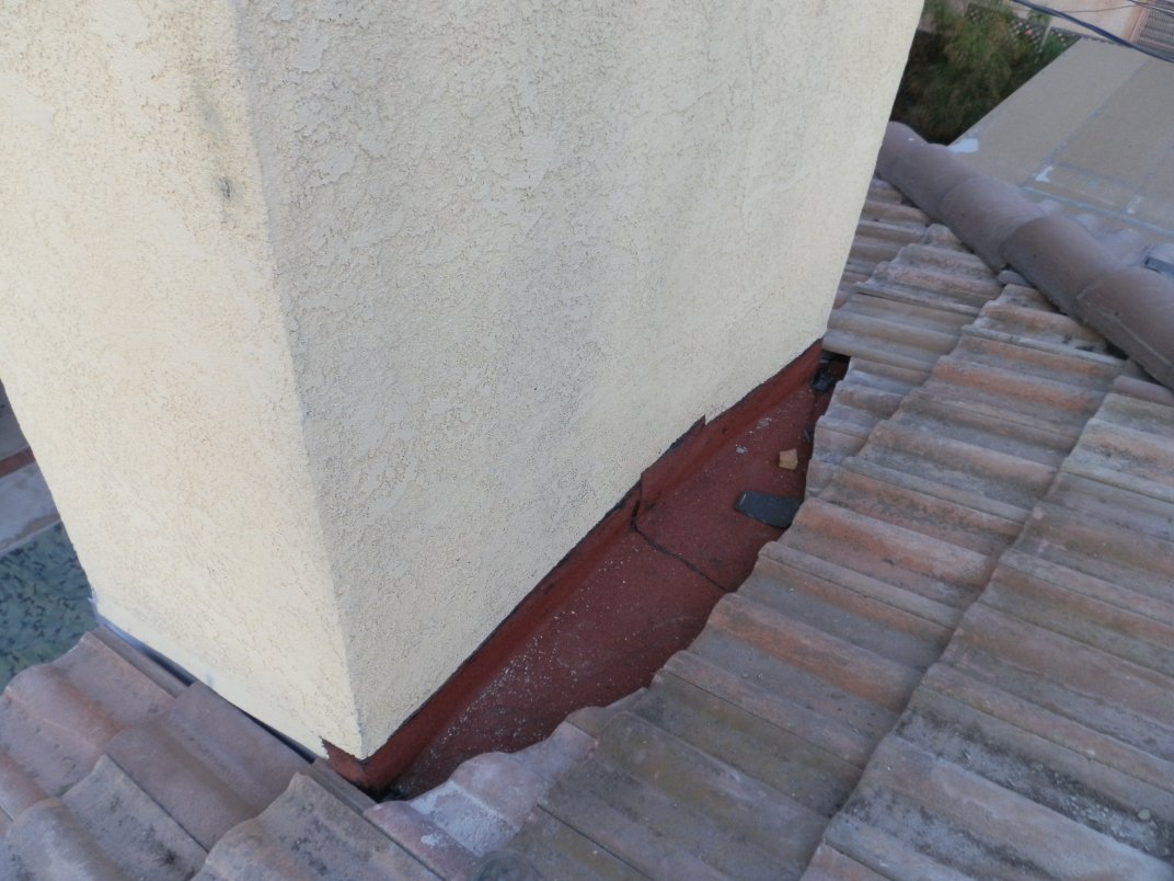 Chimney on a tile roof with flashing at its base, the area where a cricket (saddle) is built.