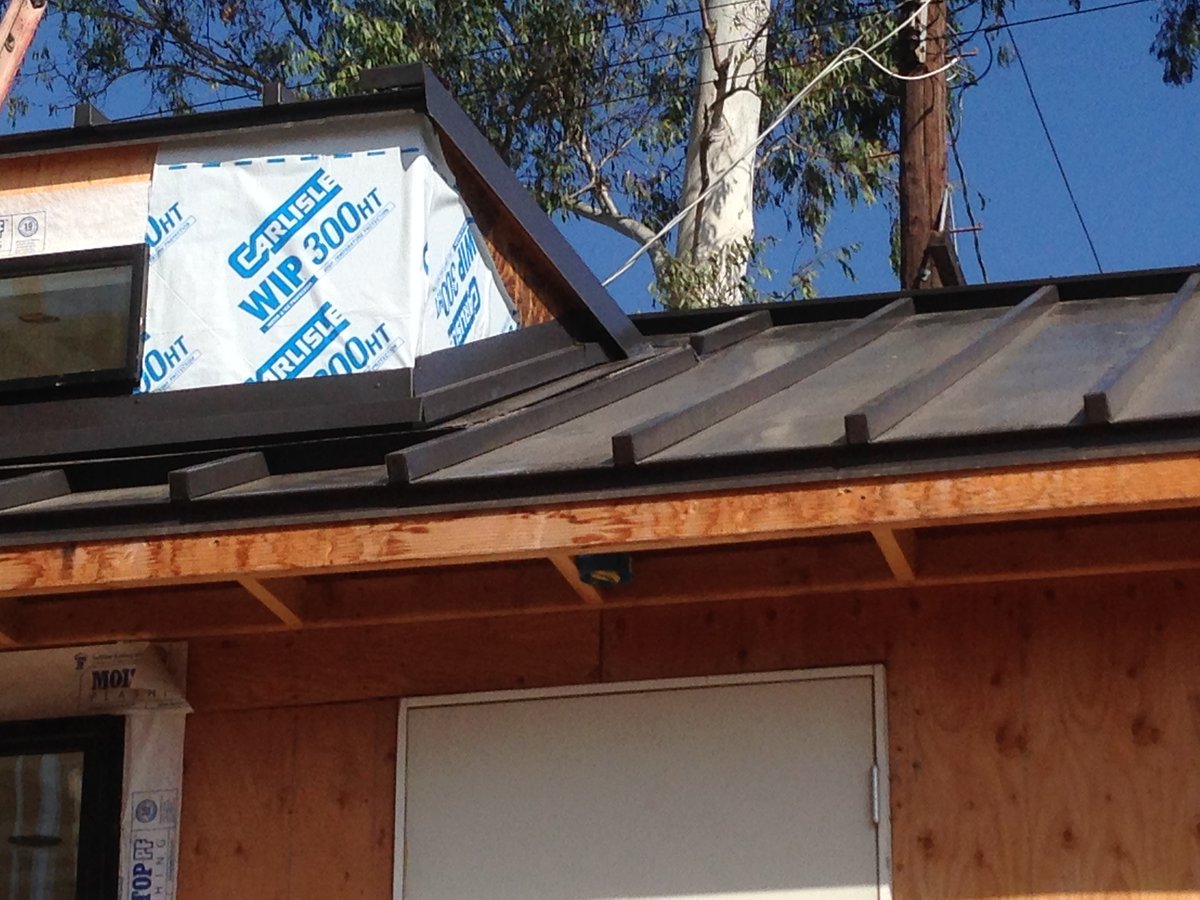 Roof eave overhanging a wall with exposed rafter tails under a metal roof.