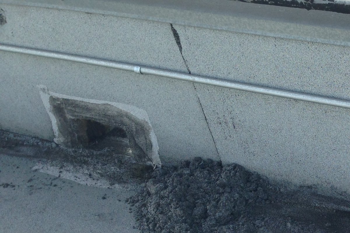 Scupper opening cut through the base of a parapet wall on a flat commercial roof.